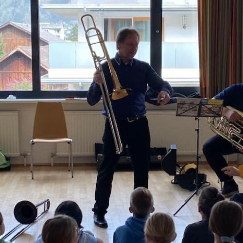 Posaune-Lehrer mit Instrument steht vor den Kindern und erklärt