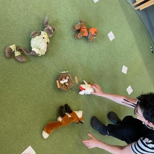 Die Lehrerin legt gerade verschiedene zur Geschichte passende Stofftiere auf den Boden