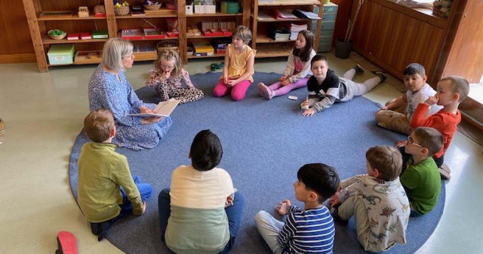 Kinder sitzen im Sitzkreis - Lehrperson liest vor
