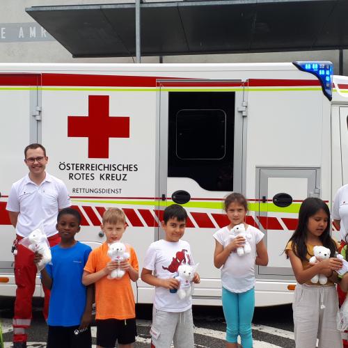 7 Kinder stehen mit Sanitätern vor dem Rettungsauto