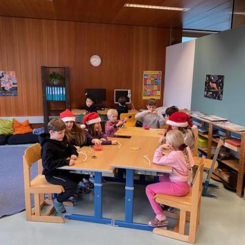 Kinder mit und ohne Weihnachtsmann-Mützen basteln am Tisch gemeinsam