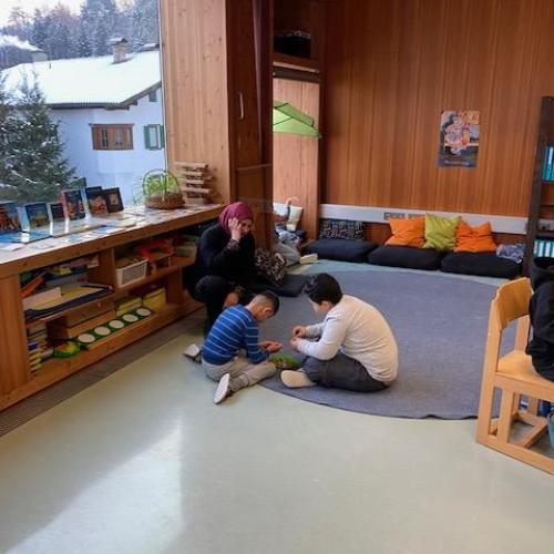 2 Kinder + Schulassistentin sitzen am Boden und arbeiten gemeinsam