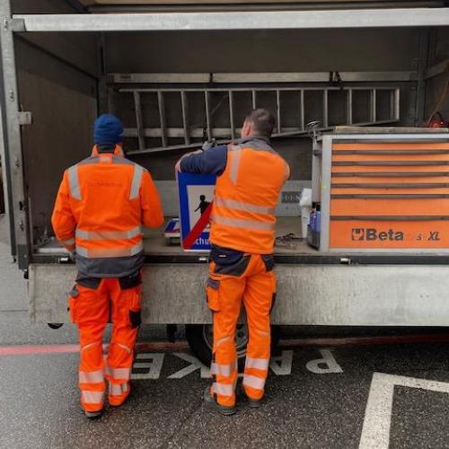 2 Straßenarbeiter in oranger Montur stehen am offenen LKW