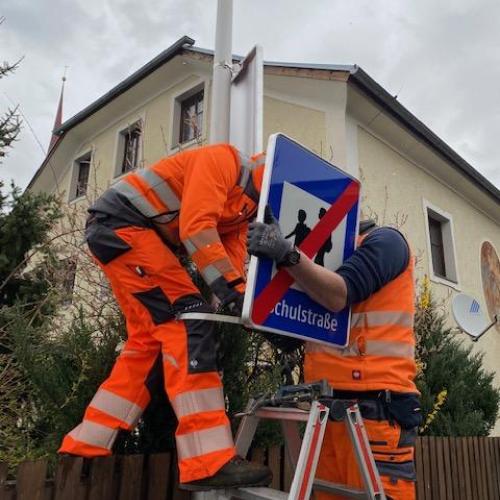 2 Männer in oranger Montur montieren die Schilder an der Straßenlaterne