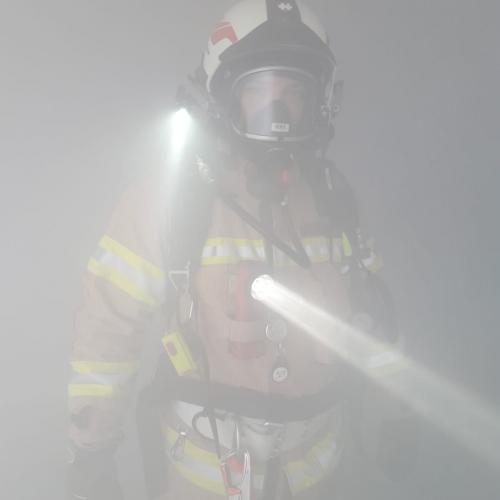 Feuerwehrmann im dichten Rauch mit Taschenlampe