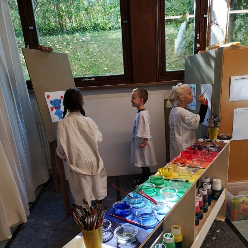 Kinder malen hinter einem Farbenregal
