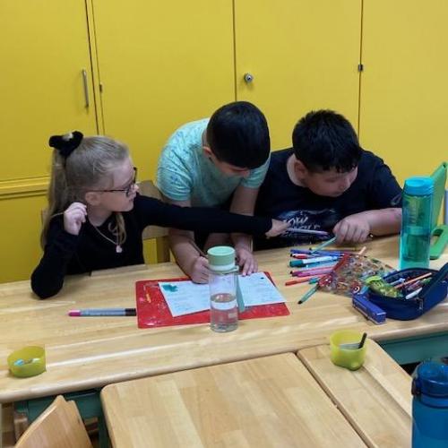 3 Kinder arbeiten gebeugt über einem Blatt