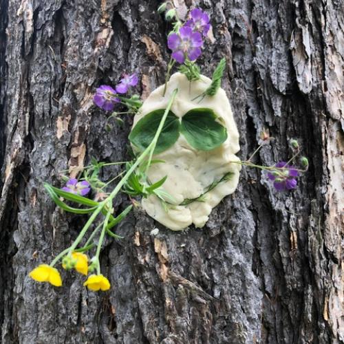 Baumgesicht aus Teig mit einem lachenden Mund, großen Augen und Blumen
