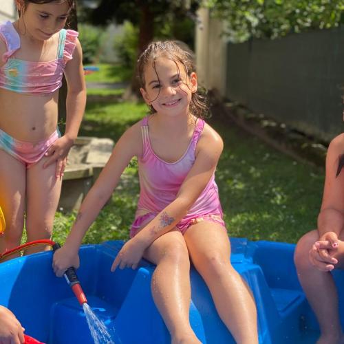 Kinder sitzen am Beckenrand und lassen das Wasser ins Planschbecken