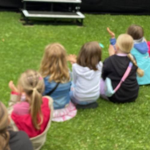 6 Kinder sitzen im Gras und bestaunen die Talente auf der Bühne
