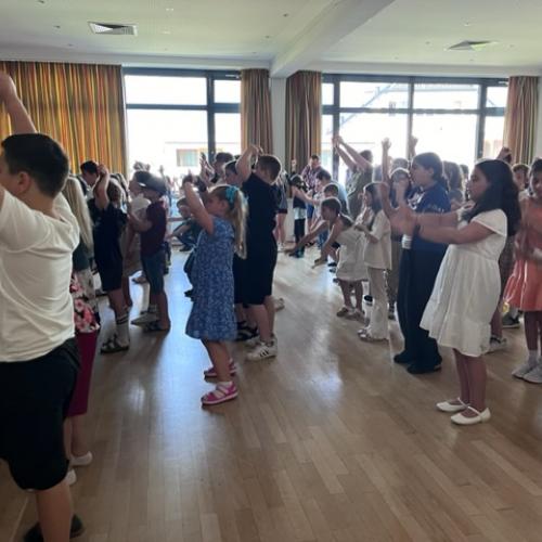 Alle Kinder der Schule stehen mit erhobenen Händen beim Singen