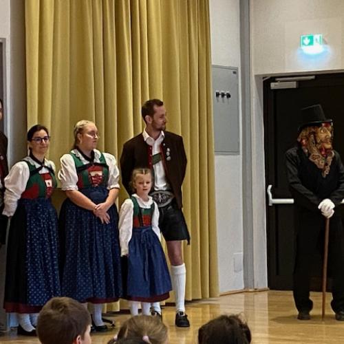 links stehen mehrere Mitglieder des Trachtenvereins in ihren schönen Trachten - rechts daneben steht die Figur "Herr" mit Maske und Zylinder