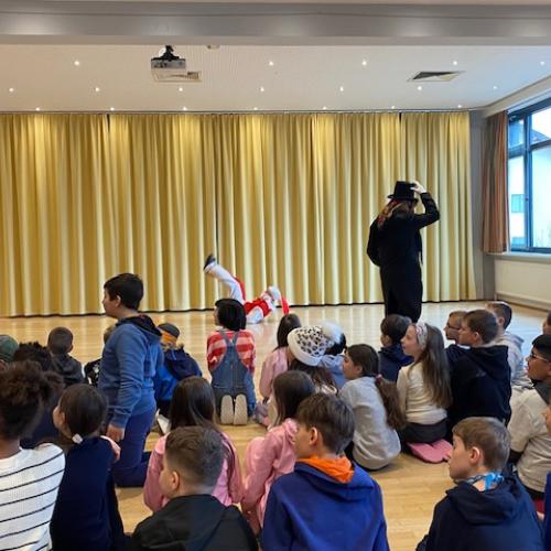 Die Kinder sitzen am Boden und sehen nach links, während der Bojatzl eine Rolle macht