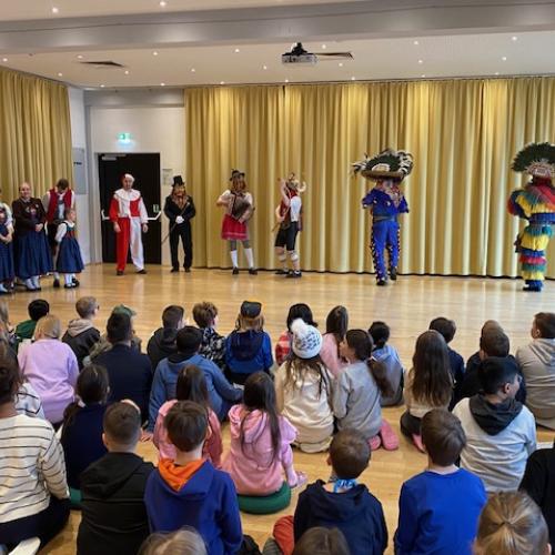 Im Hintergrund stehen die Matschgerer und der Trachtenverein - im Vordergrund sitzen Kinder am Boden