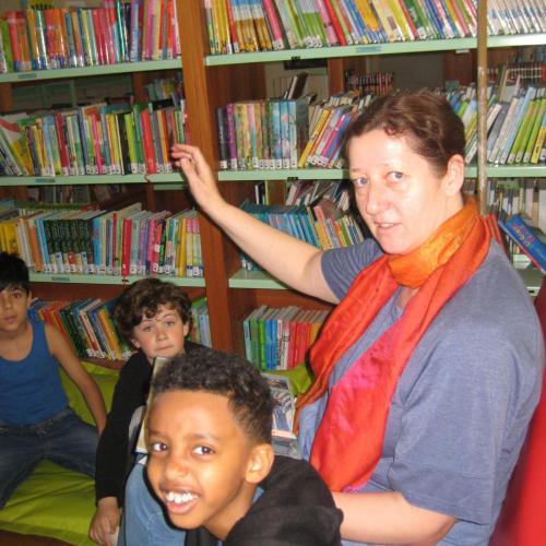 Lehrerin und Kinder sitzen vor einer Bücherwand in der Bücherei