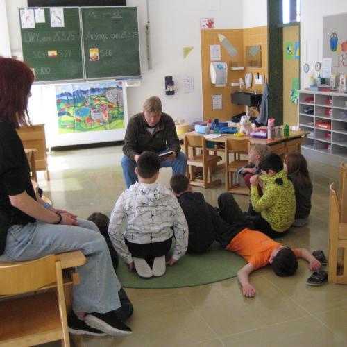 Der Herr Lehrer liest vor, währende die Kinder am Boden zuhören - ein Kind liegt
