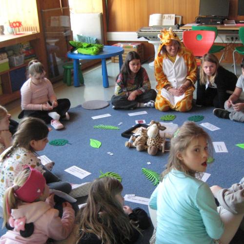 Die L sitzt als Giraffe verkleidet mitten unter den Kindern am Boden