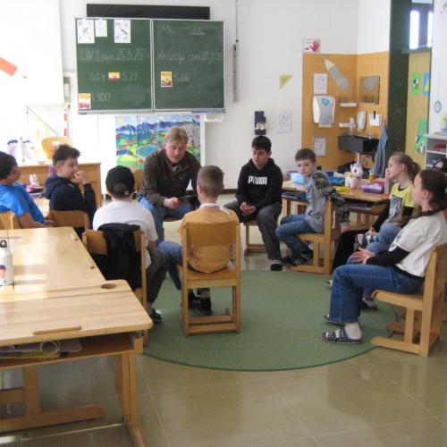 Die Kinder sitzen auf Stühlen rund um den Herrn Lehrer