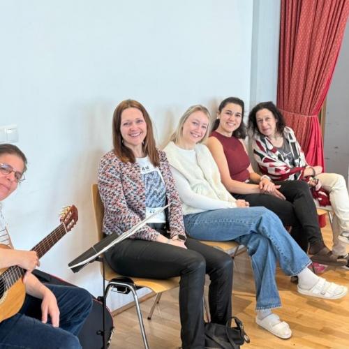 Lehrerinnen und eine Schulassistentin mit Gitarre sitzen auf der Seite und lachen