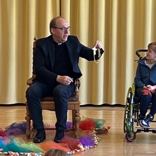 Der Bischof hält sein goldenes Kreuz hoch und gibt es an die Kinder zum Anschauen