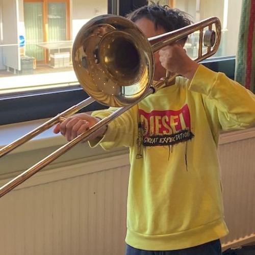 Kind mit gelbem Pullover spielt die Zugposaune