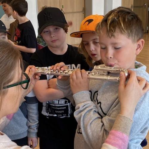 Kind bläst mit Hilfe der Lehrerin in eine gebogene Querflöte