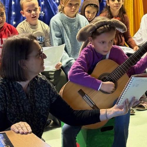 Ein Kind spielt Gitarre. Die Lehrerin hält die Noten