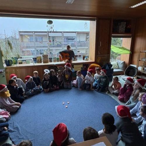 Die Kinder sitzen im Kreis und singen. Die Lehrerin spielt Gitarre