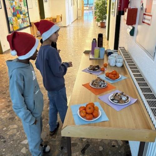 2 Kinder mit Weihnachtsmannmützen stehen vor einem kleinen Buffet