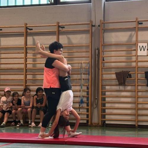 Die Lehrerin hält ein Kind, das den Handstand auf ihren Füßen macht - beide bewegen sich gemeinsam vorwärts