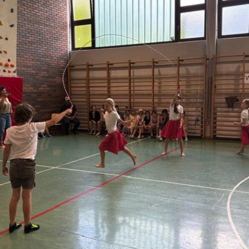Man sieht Kinder beim Langseil-Springen; die Mädchen tragen alle rote Röcke