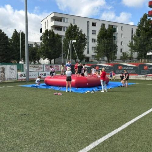 Im Hintergrund sieht man ein aufblasbares Trampolin mit vielen Kindern darauf