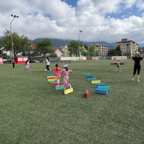 Blick auf den Platz - man sieht bunte Stangen am Boden über die Kinder springen
