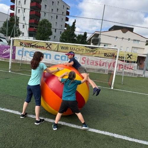 Ein Kind springt gerade auf einen riesigen Ball, während es von einer Assistentin und einem Kind unterstützt wird