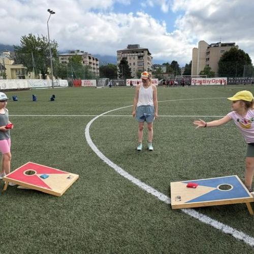 2 Kinder stehen sich mit farbigen Zielbrettern am Boden gegenüber und versuchen Sandsäckchen in die Löcher zu werfen