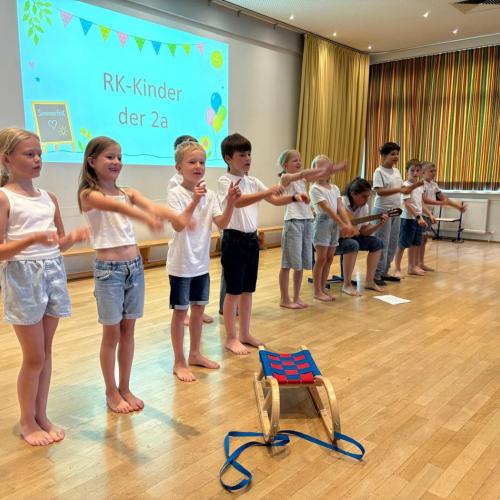Kinder tanzen zu einem Lied - im Vordergrund sieht man eine Rodel