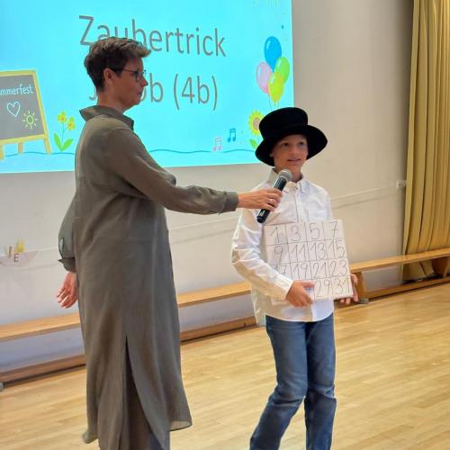 Die Direktorin hält einem Kind mit Zylinder ein Mikro hin