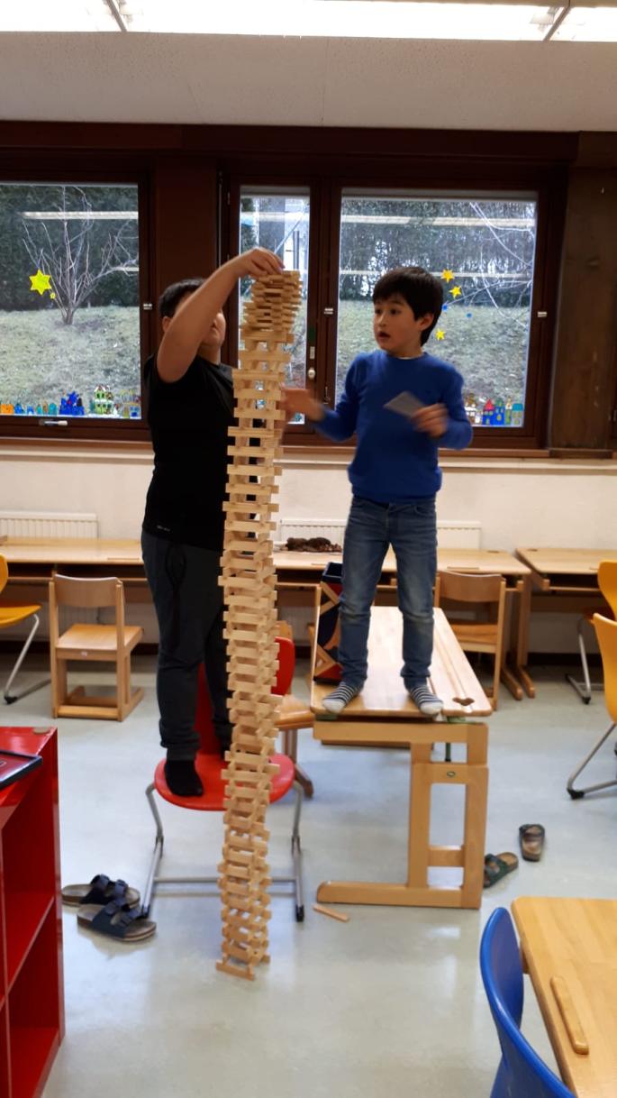 Kinder bauen einen Turm aus Hölzern und stehen dabei auf dem Tisch und Stuhl