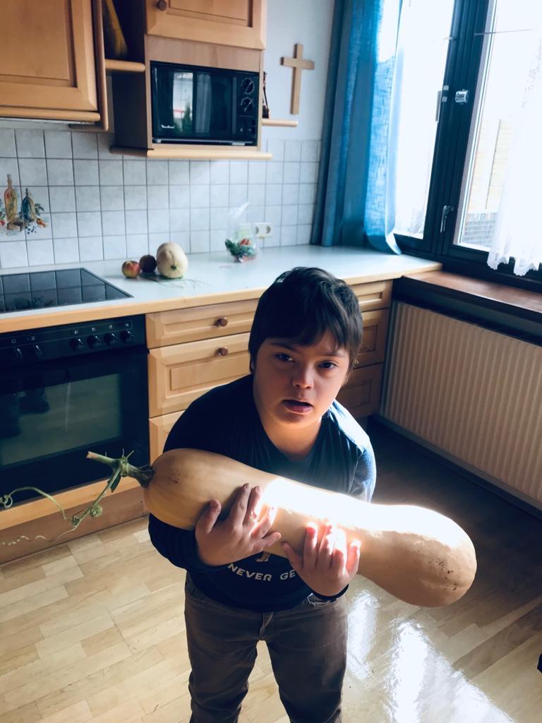 Ein Down-Kind hält einen riesige Kürbis in der Hand