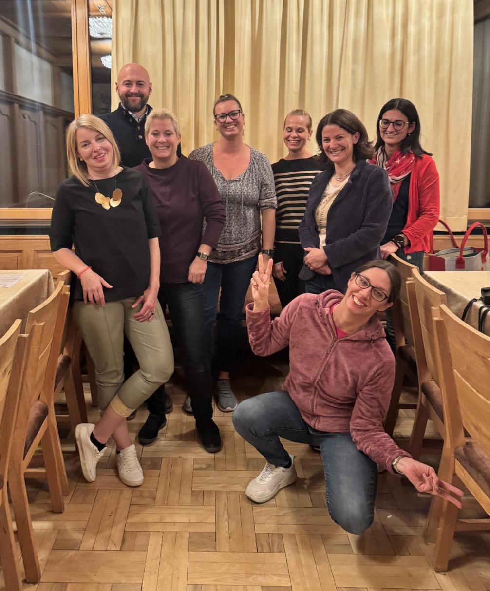 8 Personen des Elternvereins lachen in die Kamera, eine Mutter kniet mit offenen Armen vorne