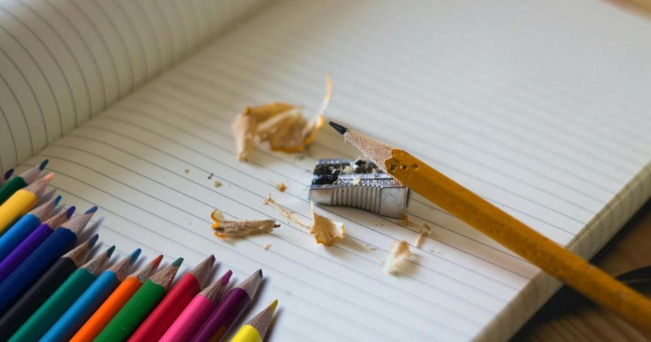 Stifte und Bleistift mit Spitzer liegen auf einem Heft