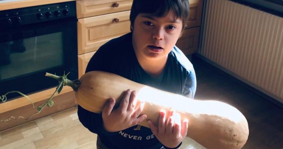 Ein Down-Kind hält einen riesige Kürbis in der Hand