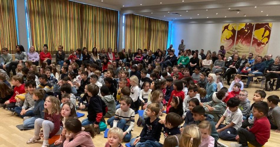 160 Kinder sitzen am Boden des Gemeindesaales; im Hintergrund Eltern auf Stühlen