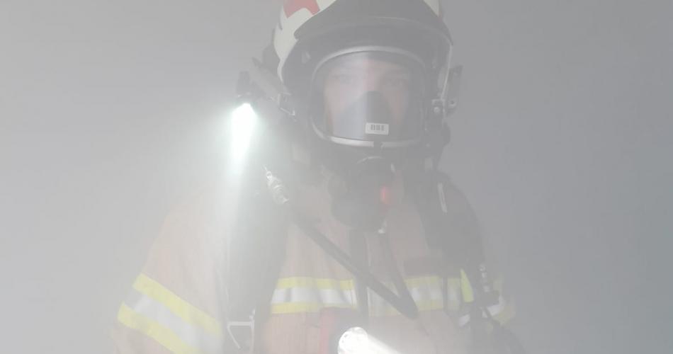 Feuerwehrmann mit Taschenlampe im Rauchnebel