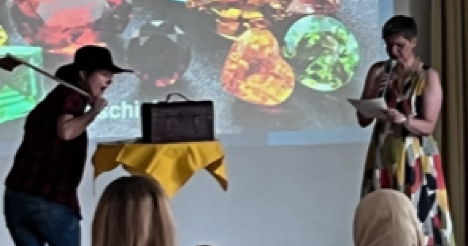 Direktorin und verkleidete Religionslehrerin stehen vor einem Bild mir großen Edelsteinen