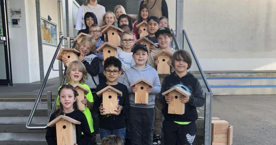 Eine Klasse steht auf der Treppe -alle Kinder halten je ein Nistkästchen in der Hand