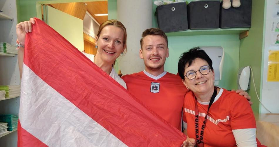 3 Lehrpersonen mit Fußballtrikots halten eine Österreich-Fahne hoch
