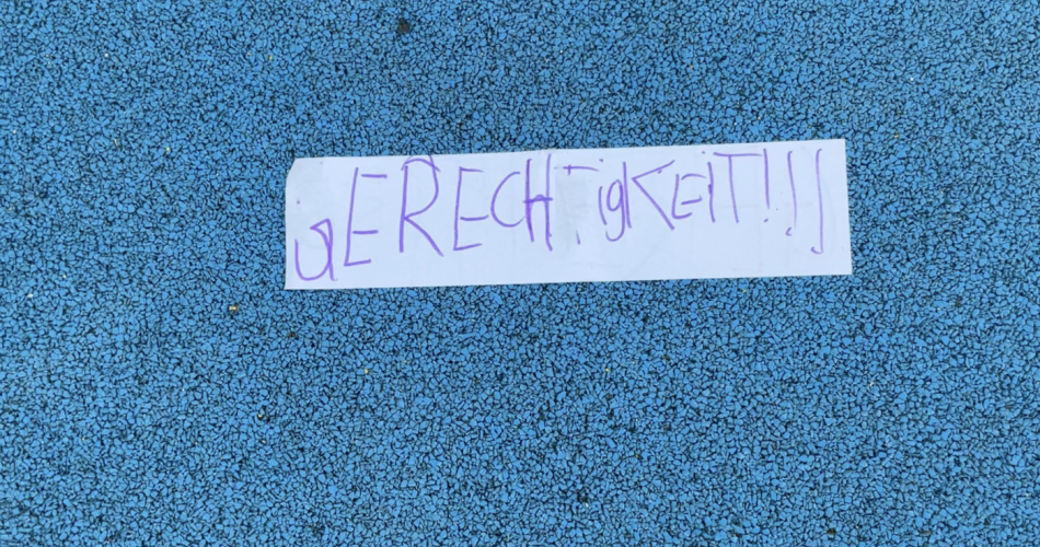 Auf blauem Hintergrund liest man ein Schild mit der Aufschrift Gerechtigkeit