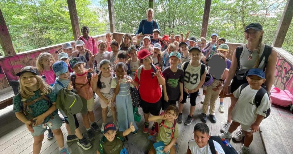 Die Kinder der 1A und 1B machen gemeinsam mit ihren Lehrpersonen ein Gruppenfoto auf einem überdachten Aussichtspunkt.