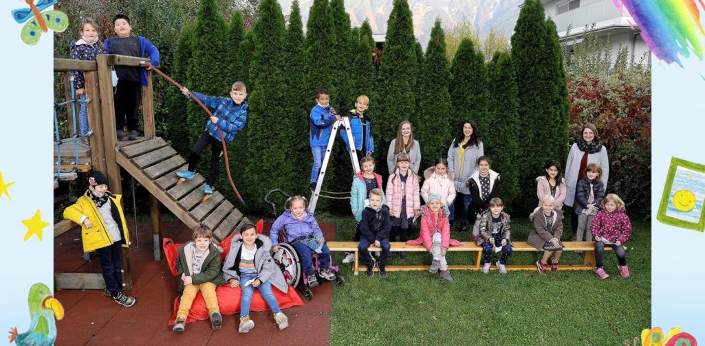 Klasse 1b sitzt im Garten und am Klettergerüst